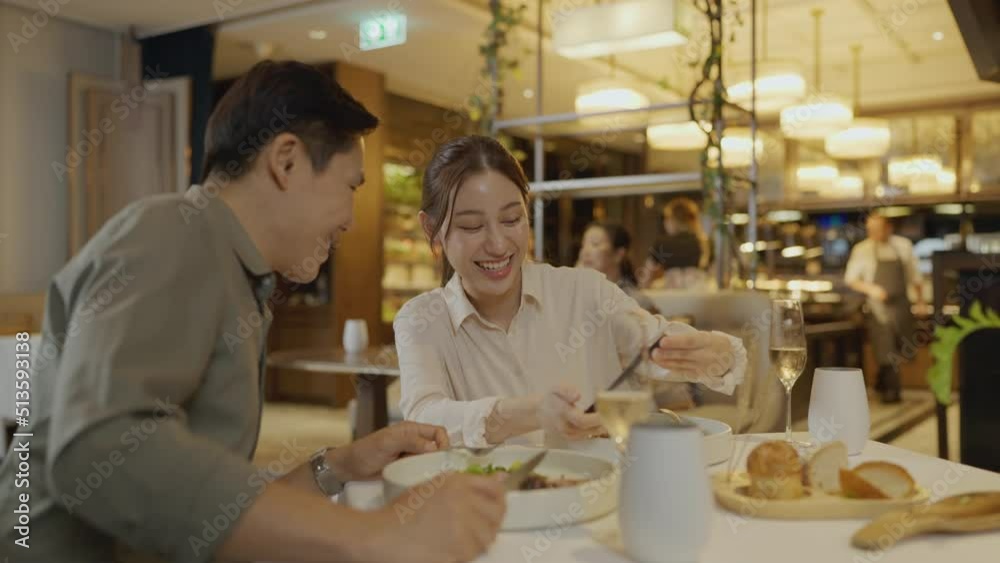 Asian couple having dinner at an upscale restaurant. Woman is taking pictures of food and showing it to her friends.