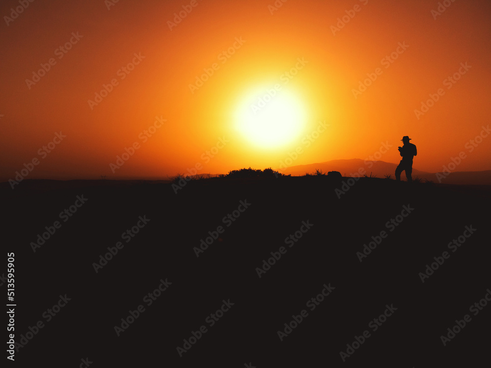 Silhouette of a man with fedora hat on sunset on a hill