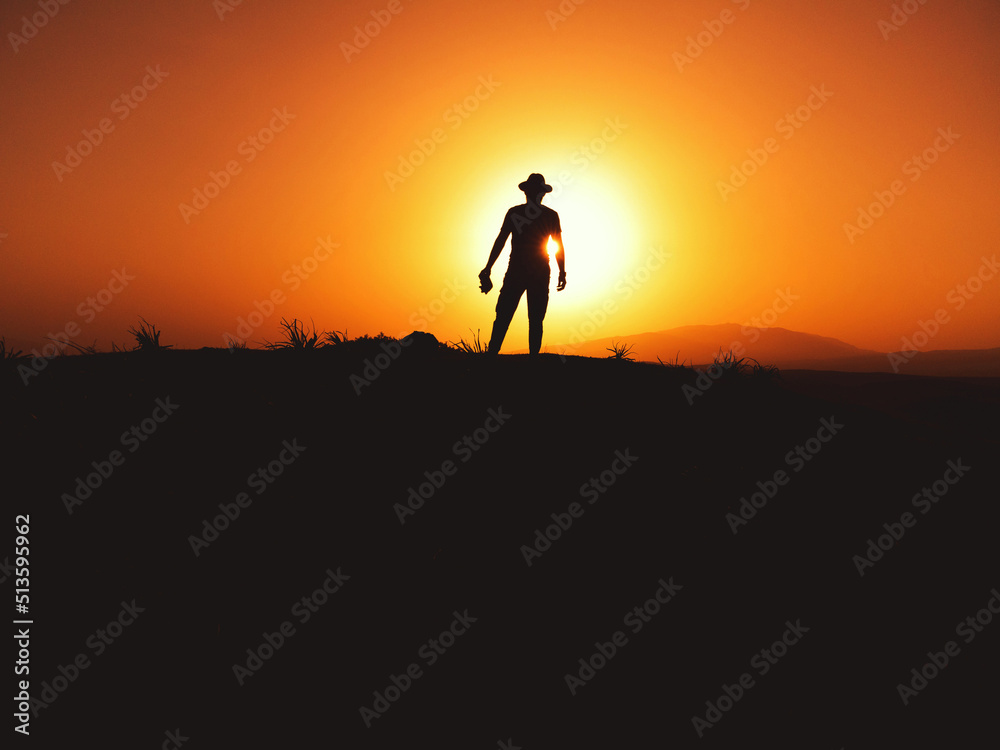 Silhouette of a man with fedora hat on sunset on a hill