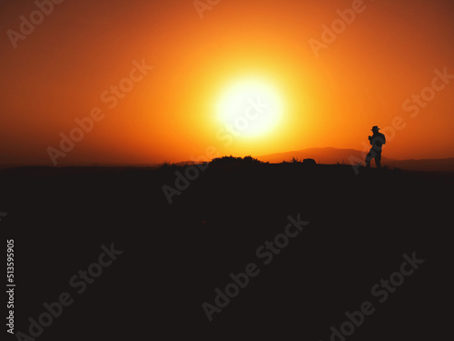 Silhouette of a man with fedora hat on sunset on a hill