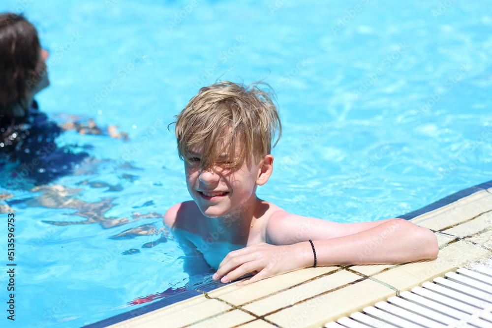 Happy young teenage boy relaxing on the side of swimming pool during summer vacation