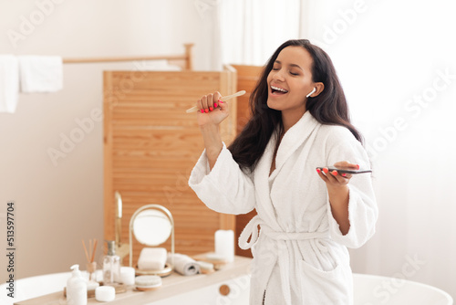 Joyful Woman Singing Holding Wooden Toothbrush And Phone In Bathroom photo