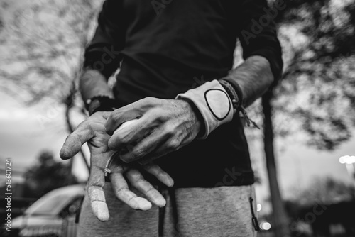 Close up of hands of a healthy and fit young latin man with wristbands holding a bag of magnesium on a street workout park with beautiful sunset sky (in black and white)