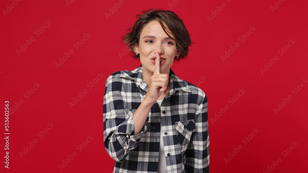Secret fun young woman 20s she wears basic white t-shirt checkered shirt look aside say hush be quiet with finger on lips shhh gesture isolated against over plain solid dark red color wall background Secret fun young woman 20s she wears basic white t-shirt checkered shirt look aside say hush be quiet with finger on lips shhh gesture isolated against over plain solid dark red color wall background