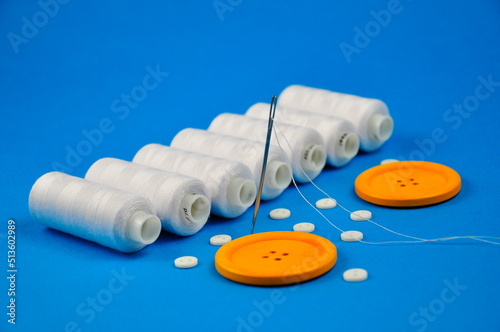 Yellow buttons, needle and spools of thread on a blue background.