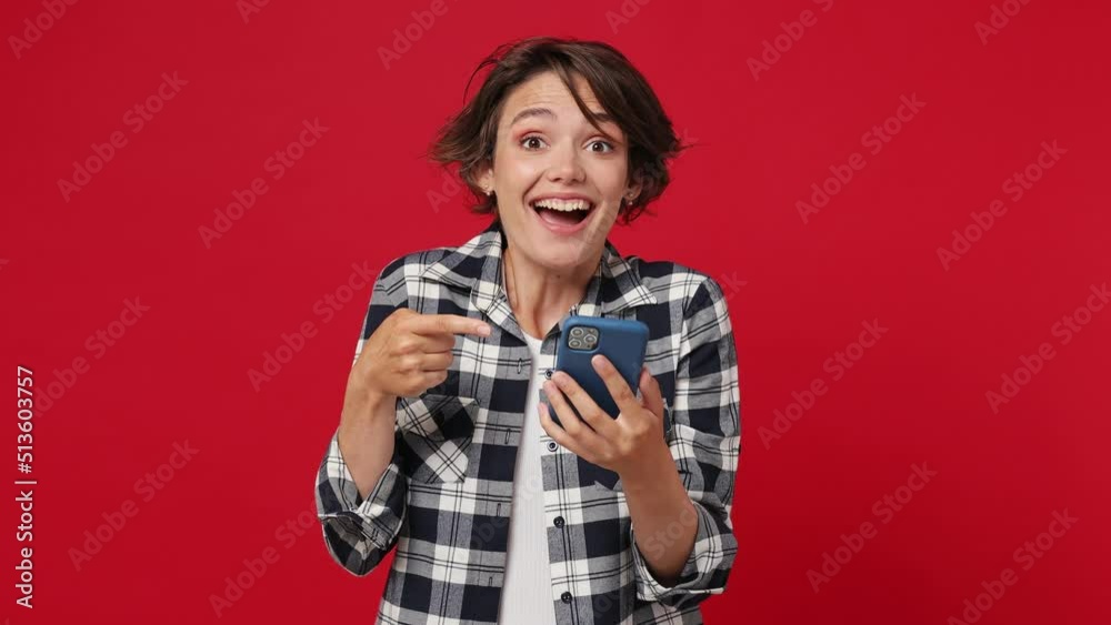 Happy excited joyful young woman 20s she wear casual clothes hold use mobile cell phone typing say wow yes just found out great big win news doing winner gesture isolated on plain red color background Happy excited joyful young woman 20s she wear casual clothes hold use mobile cell phone typing say wow yes just found out great big win news doing winner gesture isolated on plain red color background