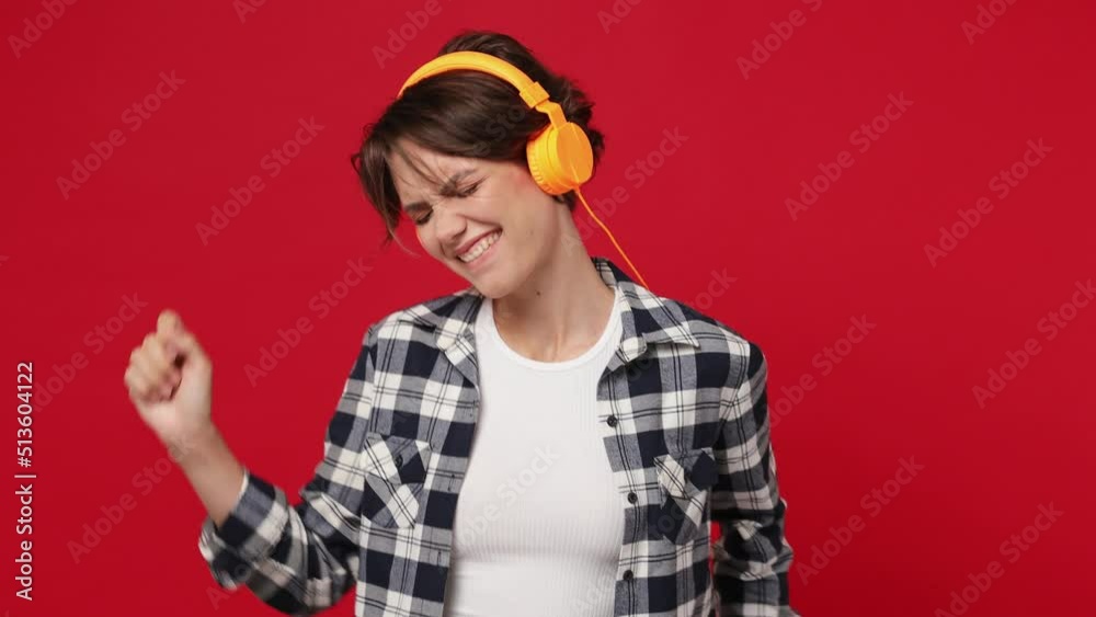 Vivid cheerful woman 20s she wearing basic white t-shirt checkered shirt listen music in headphones dance fooling around have fun enjoy relax isolated on plain solid dark red color background studio Vivid cheerful woman 20s she wearing basic white t-shirt checkered shirt listen music in headphones dance fooling around have fun enjoy relax isolated on plain solid dark red color background studio