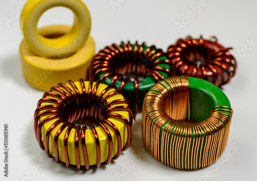 Small family of inductive chokes on a white background. Inductive component, copper wire coil, yellow toroid - macro picture. 