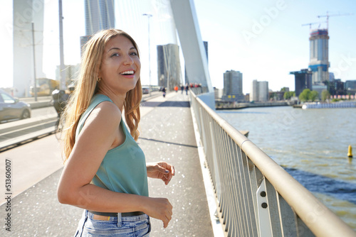 Confident young smiling woman walking on Erasmus Bridge turns around at sunset in Rotterdam, Netherlands