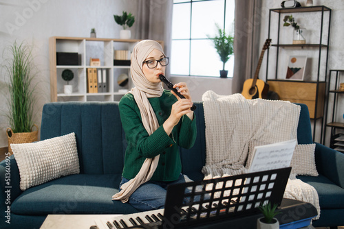 Fototapeta Portrait of young arab female with hijab playing on flute