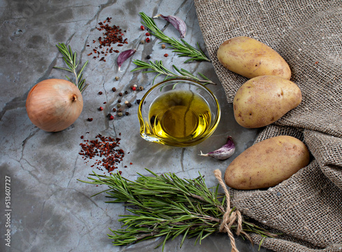 Ingredients for delicious fried or baked potatoes: potatoes, onions, garlic, olive oil, rosemary, dried tomatoes, multicolored pepper. Natural background.
