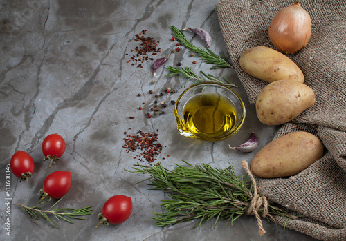 Raw potatoes, rosemary, olive oil, colorful peppers, garlic, onion, fresh and dried tomatoes are the ingredients for delicious baked potatoes in a rustic way. Natural background with a space for text