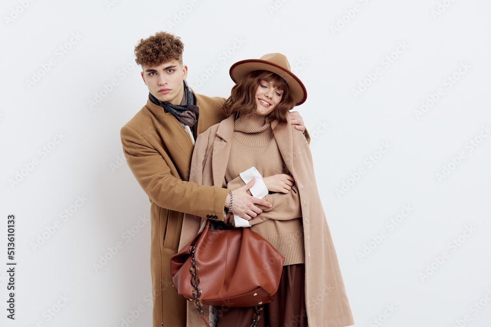 a happy couple in love is standing in beige stylish autumn coats on a white background and a man is holding a woman's hands smiling pleasantly a happy couple in love is standing in beige stylish autumn coats on a white background and a man is holding a woman's hands smiling pleasantly