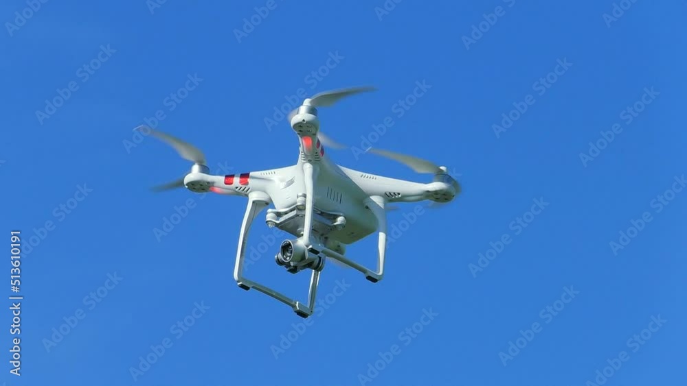 White quadcopter fly in the blue sky. Drone is flying high over the terrain. White quadcopter fly in the blue sky. Drone is flying high over the terrain.