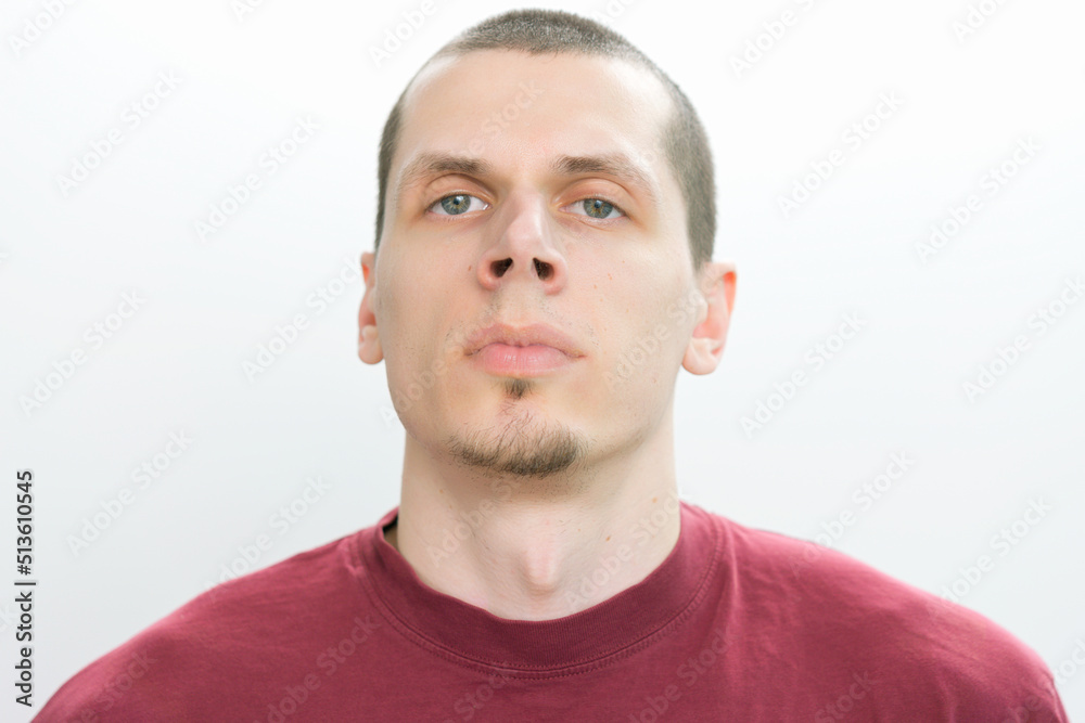 Obraz premium A confident man in a red t-shirt looks straight on a white background. Modern. Studio. White. Young. Casual. Fashion. Lifestyle. Authority. Concentration. Hold