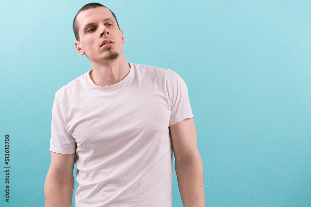 A confident man in a white t-shirt looks on the side way and holds his head raised on a blue background. Modern. One. Studio. White. Young. Casual. Fashion. Lifestyle. Authority. Concentration. Hold A confident man in a white t-shirt looks on the side way and holds his head raised on a blue background. Modern. One. Studio. White. Young. Casual. Fashion. Lifestyle. Authority. Concentration. Hold