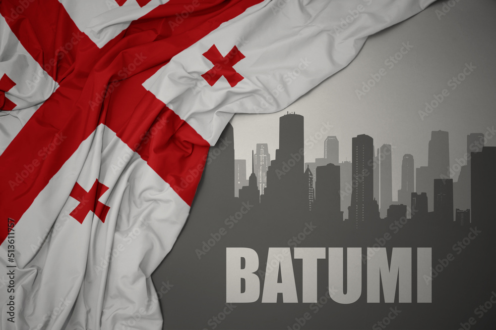 Fototapeta premium abstract silhouette of the city with text Batumi near waving national flag of georgia on a gray background.