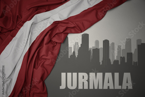 abstract silhouette of the city with text Jurmala near waving national flag of latvia on a gray background.