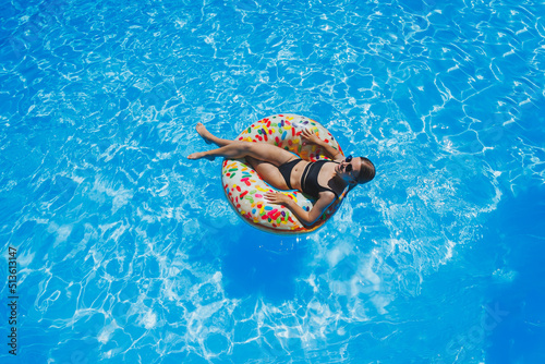 Beautiful woman in sunglasses in the pool floats on an inflatable swimming ring in a black swimsuit, summer photo, swimming photography, summer woman photos