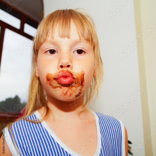 Little girl with a dirty mouth is eating Alpine chocolate. Lips with a bow.