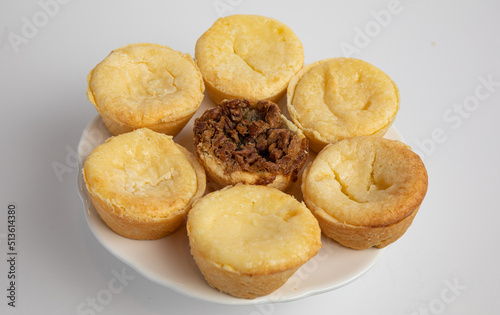 Yellow cream tarts on a plate with a pecan tart in the middle, white background