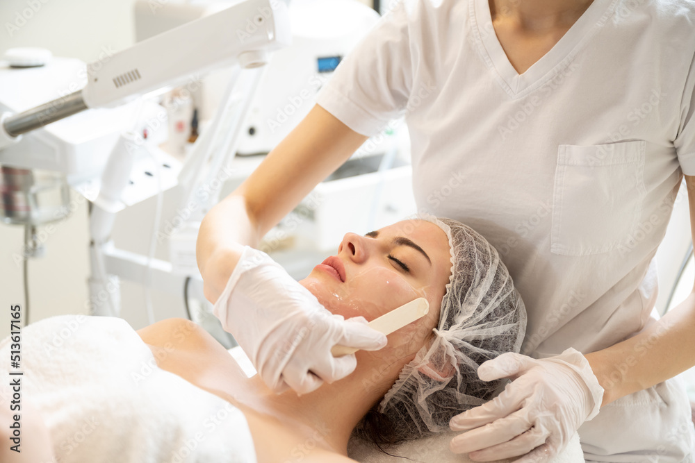 Obraz premium Beautician applying hydro gel mask on the young woman face, before laser treatment in beauty salon.