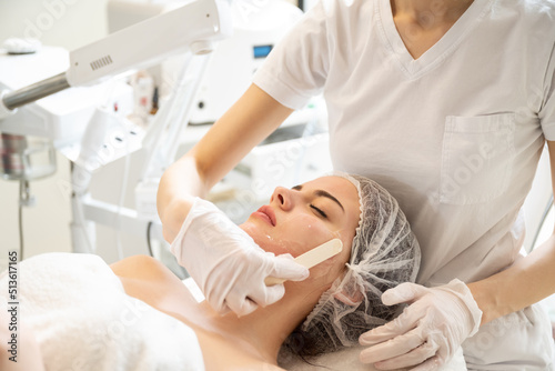 Beautician applying hydro gel mask on the young woman face, before laser treatment in beauty salon.