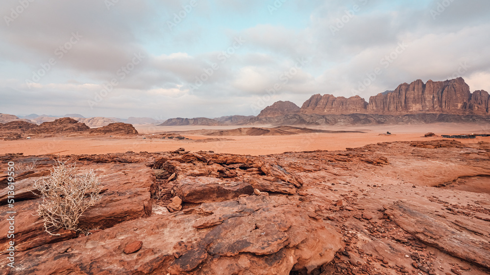 Rocky scenery in Wadi Rum desert during overcast morning, camp tents visible in distance