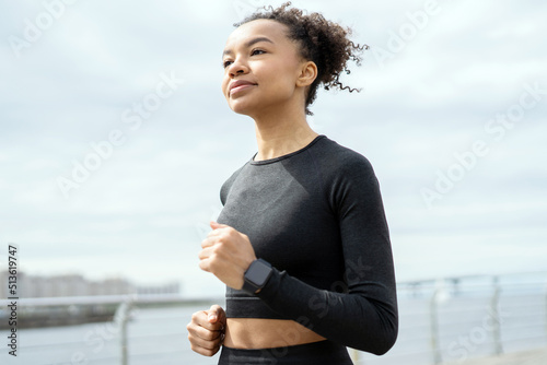 A woman runs fitness training on the street, active exercises in a sports uniform, fitness watch on her hand
