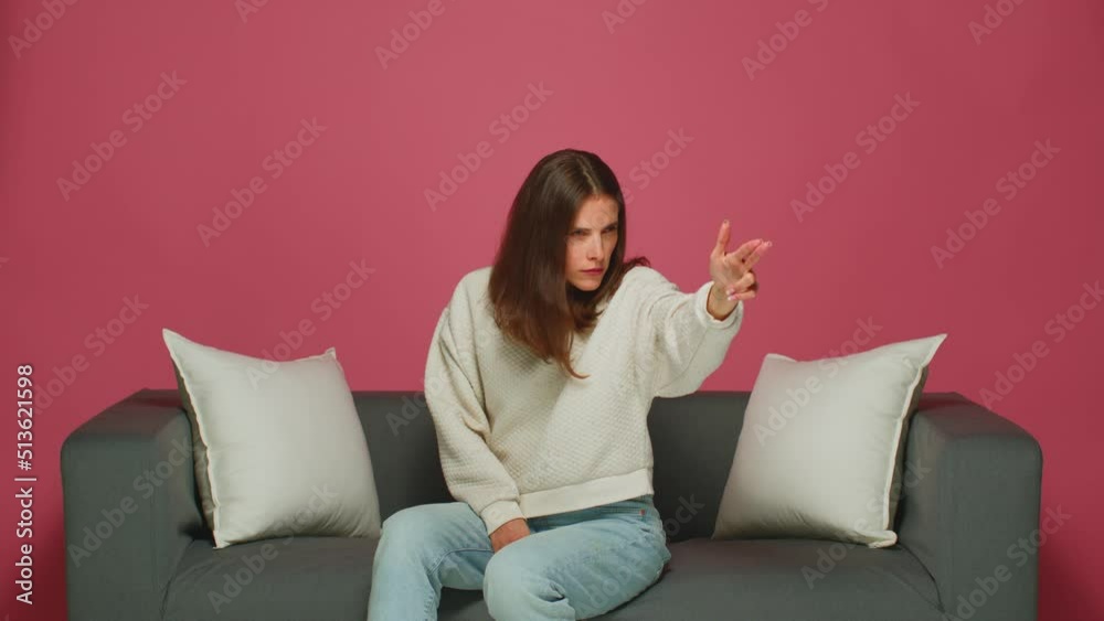 Cool young girl searching for target with gun gesture. Woman shooting with hand pistol to camera, sitting on couch Cool young girl searching for target with gun gesture. Woman shooting with hand pistol to camera, sitting on couch