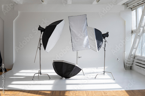 Professional lighting equipment, flashes, c-stands on a cyclorama in modern photo studio with a huge windows. Octabox, stripbox, softbox, buety plate and other stuff for photography. photo