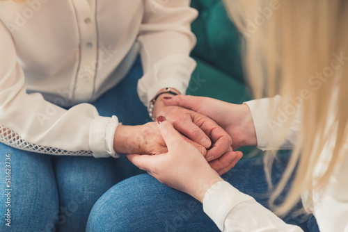 Close-up inner shot of two unrecognizable women sitting on a green couch holding their hands  supporting each other. High quality photo