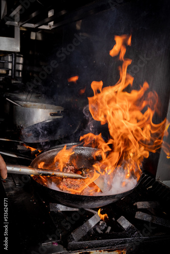 Manos que cocinan en un restaurant, con sarten sobre fuego. Salteado de carnes