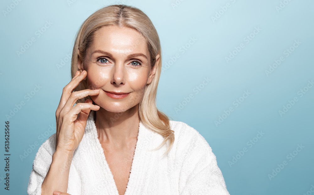 Fototapeta premium Beautiful 50s mid aged mature woman looking at camera isolated on blue. Mature old lady close up portrait. Healthy face skin care, middle age skincare cosmetics, cosmetology concept