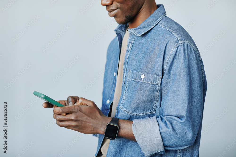 Minimal cropped shot of young black man holding smartphone and typing messages against grey background, copy space Minimal cropped shot of young black man holding smartphone and typing messages against grey background, copy space
