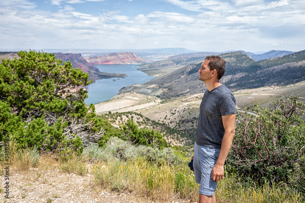 Man standing looking at view over Sheep Creek Overlook in Manila, Utah near Flaming Gorge National Park with cloudy valley and river Man standing looking at view over Sheep Creek Overlook in Manila, Utah near Flaming Gorge National Park with cloudy valley and river