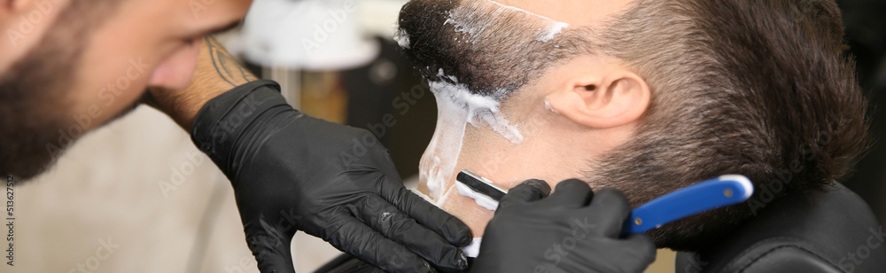 Professional hairdresser shaving client with straight razor in barbershop, closeup. Banner design