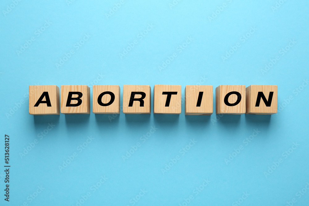 Fototapeta premium Word Abortion made of wooden cubes on light blue background, flat lay