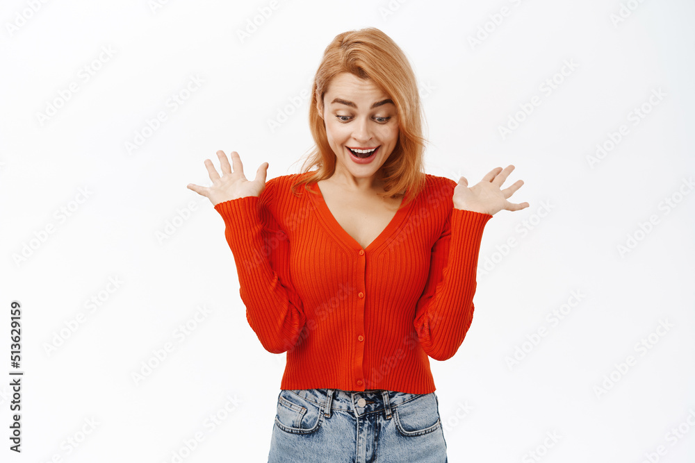 Woman looks surprised at gift below. Girl screams amazed and looks down, stands over white background Woman looks surprised at gift below. Girl screams amazed and looks down, stands over white background