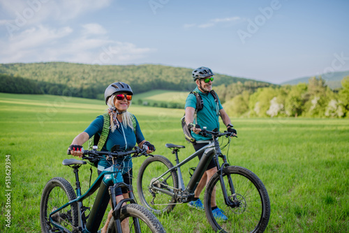 Active senior couple with electric bicycles on meadow in summer, healthy lifestyle concept.