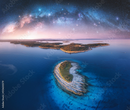 Fototapeta Naklejka Na Ścianę i Meble -  Milky Way arch and beautiful yachts and boats on the sea bay at summer night. Kamenjak, Croatia. Space. Top view of arched milky way, starry sky, sailboats, lagoon, clear blue water, forest. Travel