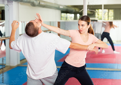 Young woman paired up with male partner in self defense training, practicing basic palm strike..