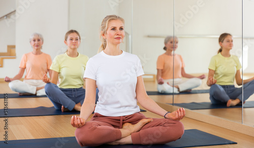 Group of active women and teen girl doing yoga Padmasana exercise, Lotus pose