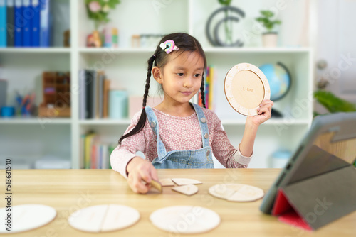 Cute asian 6 years old asian little girl is studying time by wooden clock online classroom, concept of creativity, learning, virtual, connect and technology, montessori, education and kid development.