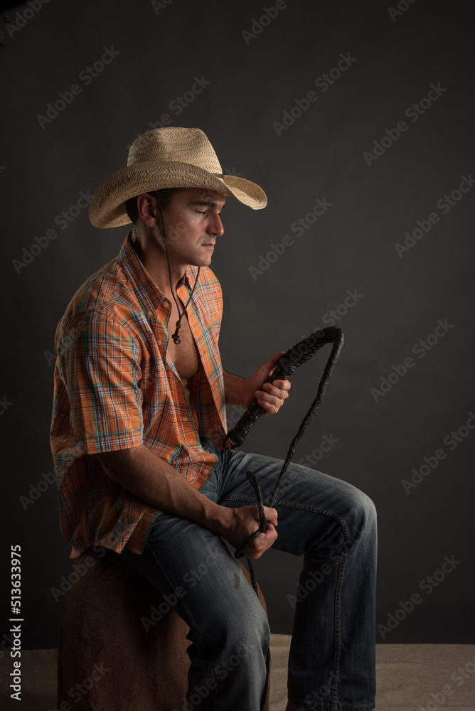The attractive cowboy man is posing in a studio for the photo.