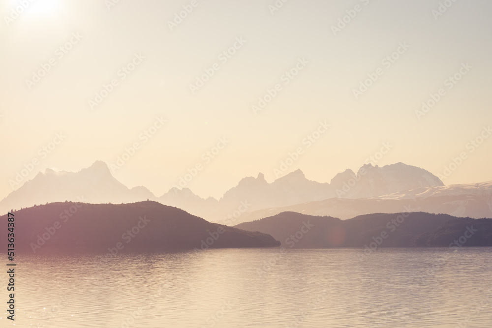 siluetas de cerros y montañas en la distancia en lago brumoso con colores de medio día magentas 
