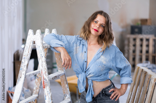 Attractive young woman in denim shirt and shorts posing next to stepladder in a refurbished room