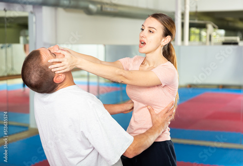 Caucasian woman performing eye-gouging move while sparring with man in gym during self-defence training.