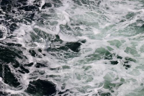 Stern waves with white foam tips on greyish blue sea water, photo taken from aboard ship. Selective focus