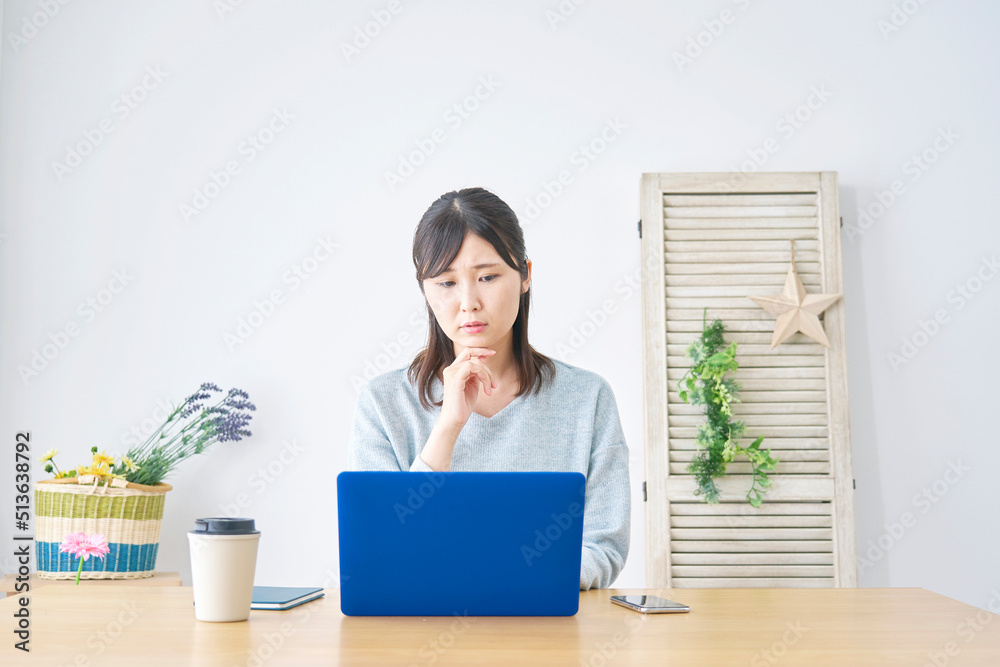 リビングでノートパソコンの前で悩む女性